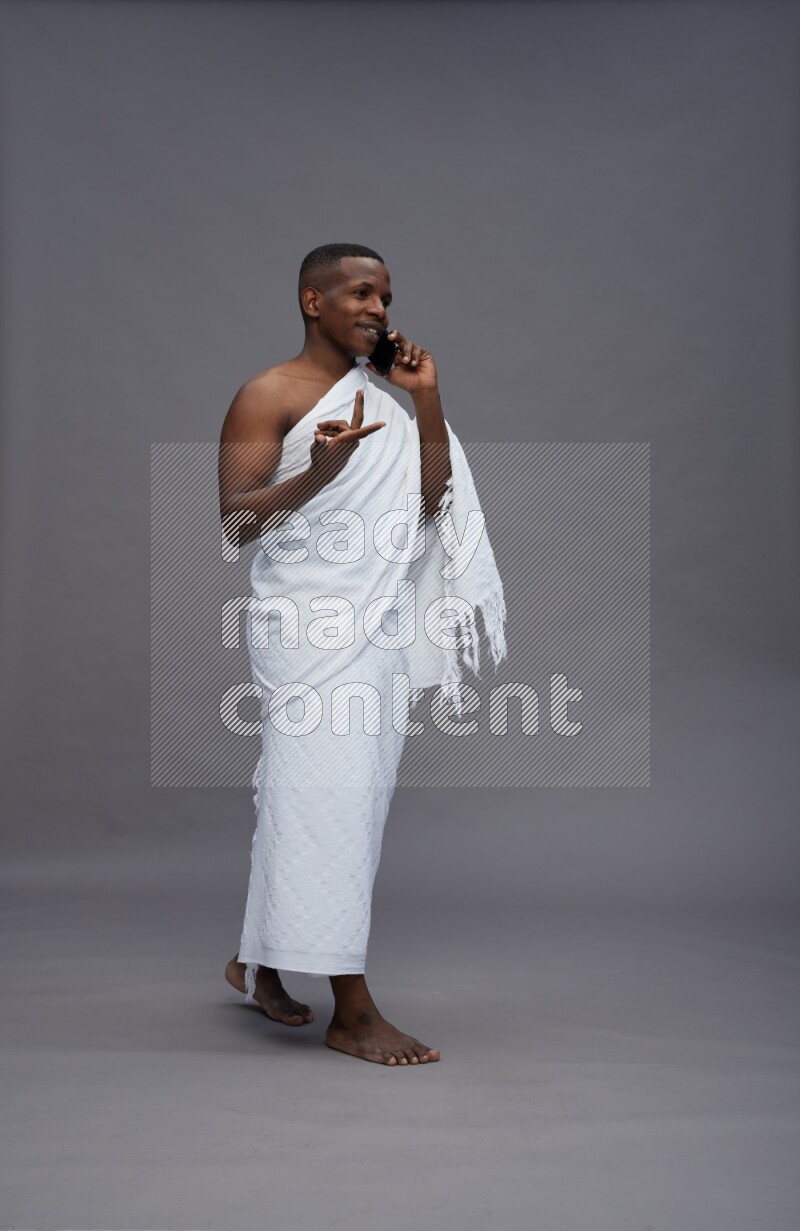 A man wearing Ehram Standing talking on phone on gray background