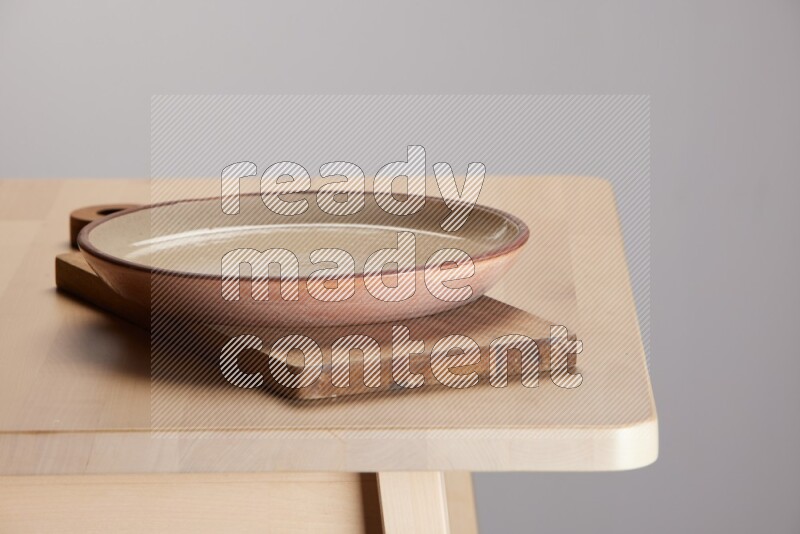multi-colored pottery Plate placed on a  wooden rectangular cutting board on the edge of wooden table