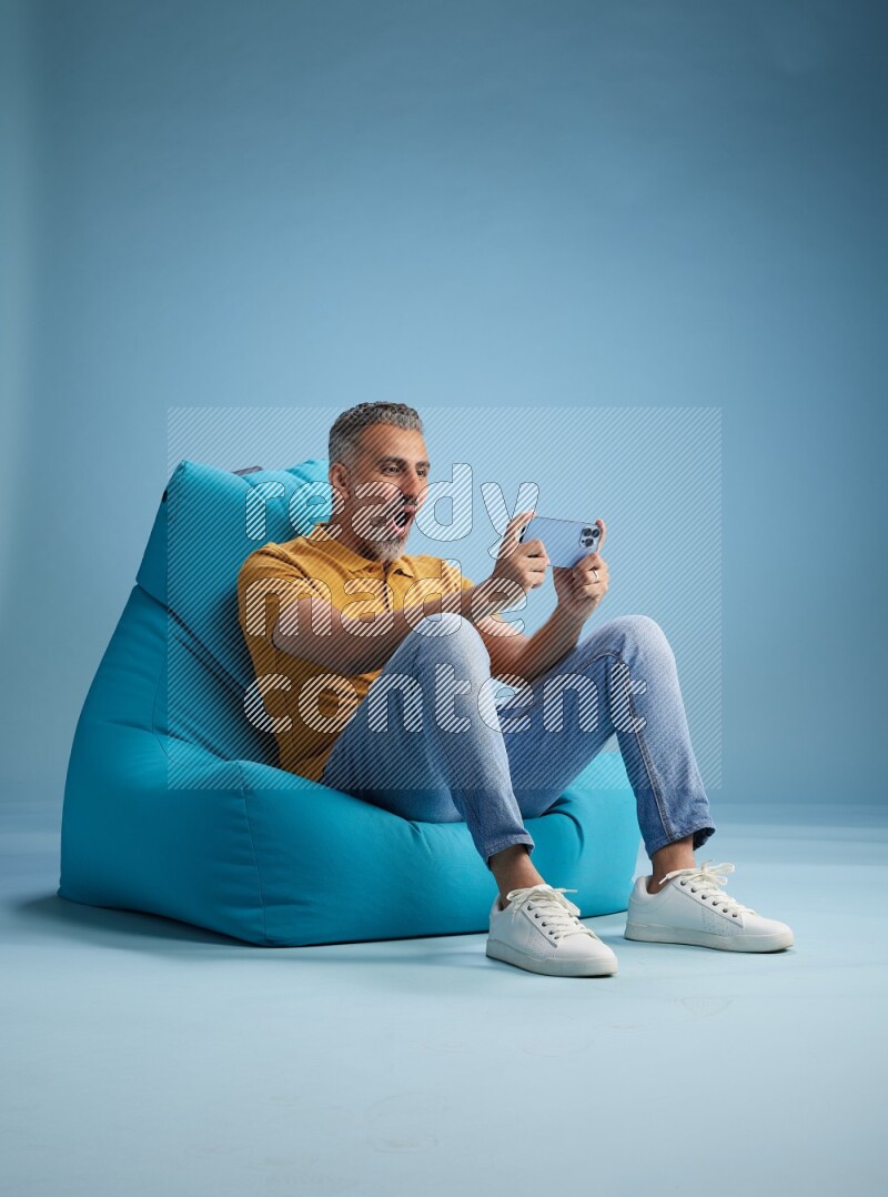A man sitting on a blue beanbag and playing on phone