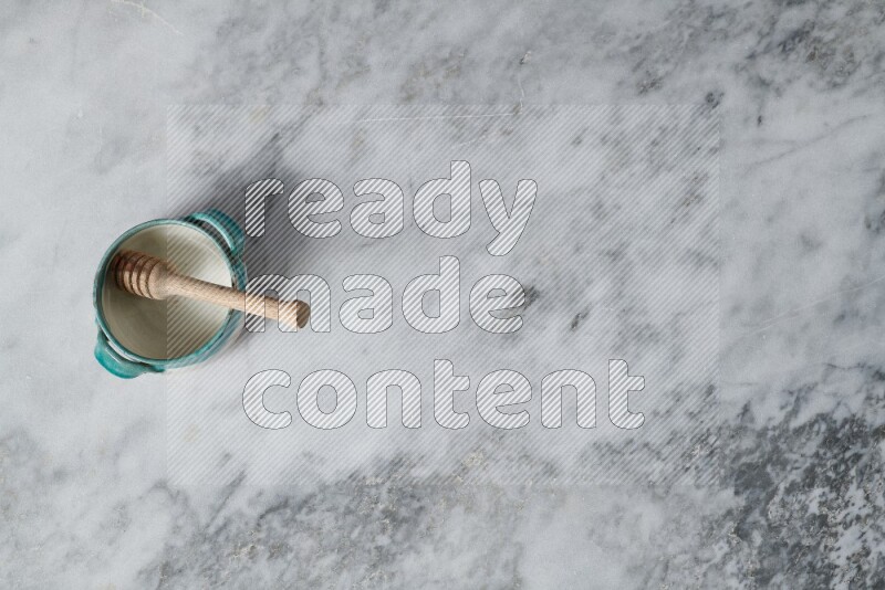 وعاء فخاري متعدد الألوان مع ملعقة عسل خشبية بداخله على خلفية من الرخام الرمادي