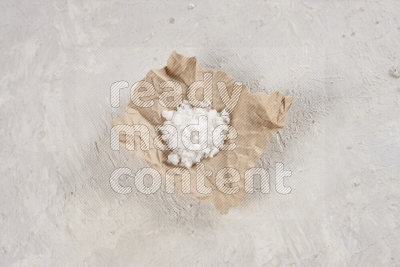 A crumpled piece of paper full of white salt on white background