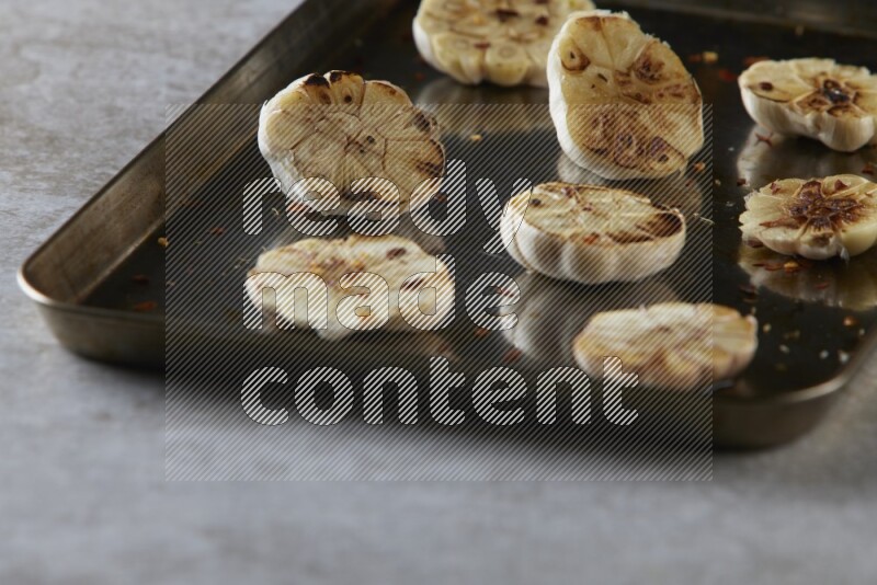 half's roasted garlic in a stainless tray on a grey textured countertop