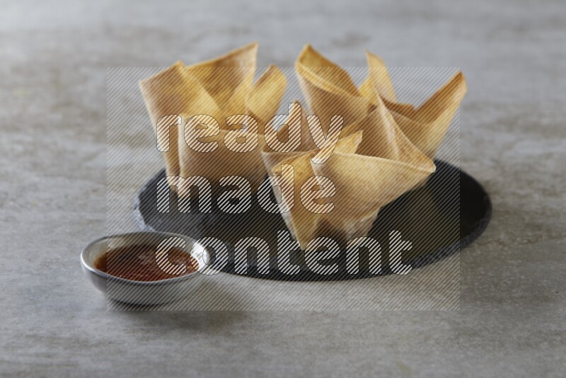 wonton cups with soy sauce ramkin on circle slate on grey textured counter top