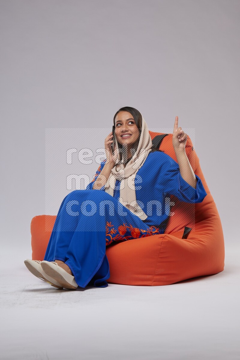 A Saudi woman wearing Jalabiya sitting on an orange beanbag and talking on the phone