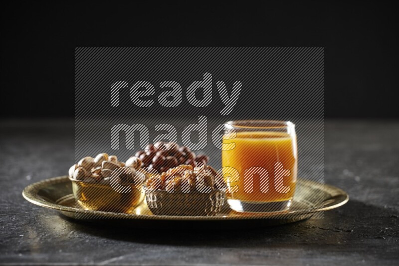Nuts in metal bowls with qamar eldin on a tray in dark setup