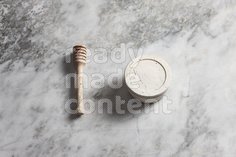 White pottery bowl with wooden honey dipper on the side on grey marble background