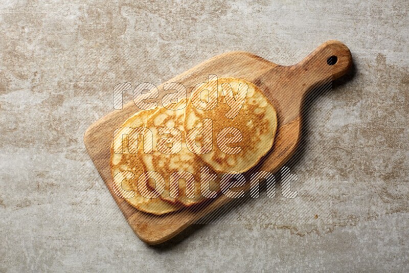 Three stacked plain pancakes on a wooden board on beige background