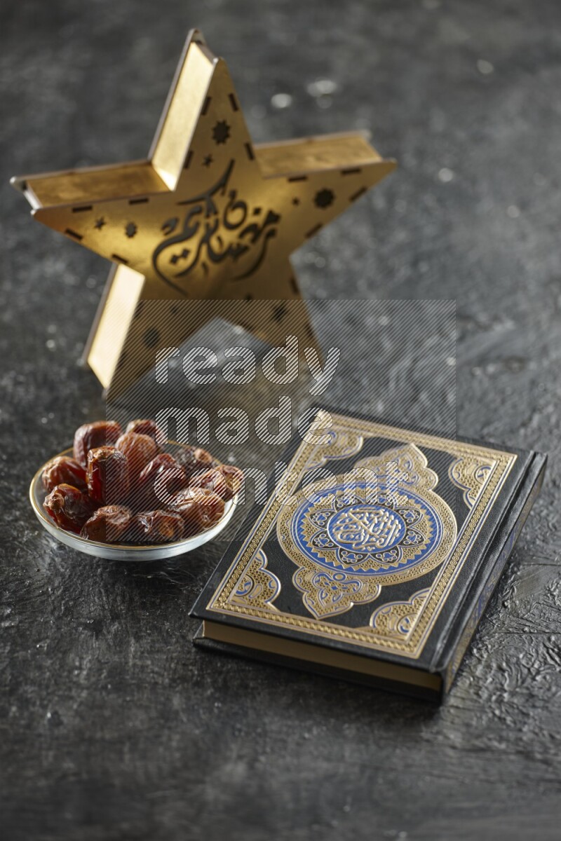 A wooden golden star lantern with different drinks, dates, nuts, prayer beads and quran on textured black background
