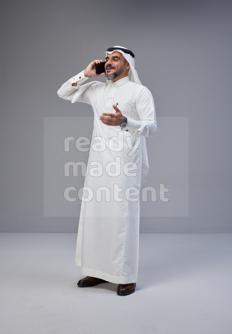 Saudi man Wearing Thob and white Shomag standing talking on phone on Gray background