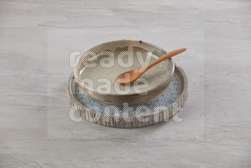 multi color pottery round dish on top of multi color round ceramic plate and spoon, on grey textured countertop