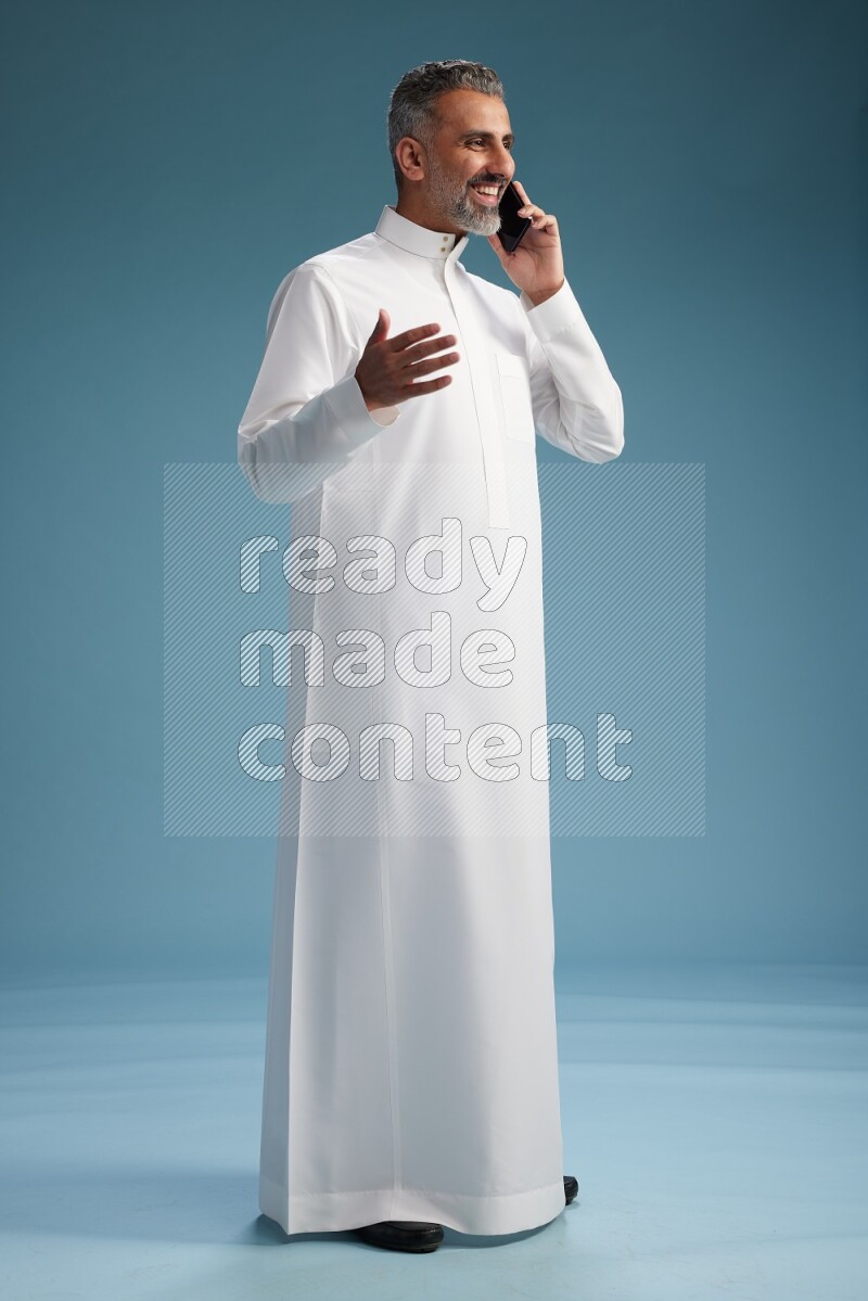 Saudi man wearing thob talking on the phone on blue background