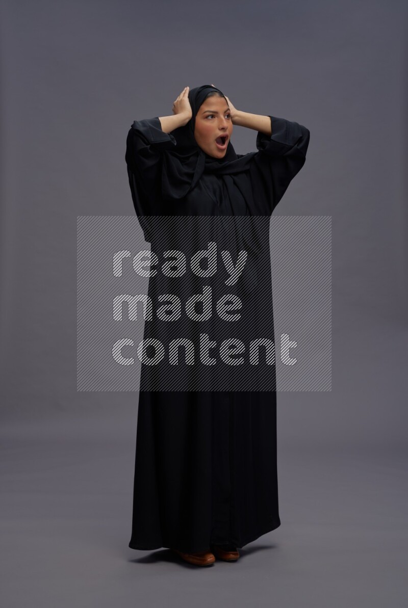 Saudi woman wearing Abaya standing hands behind head on gray background