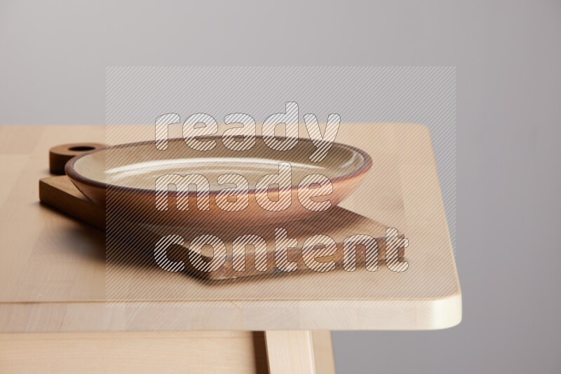 multi-colored pottery Plate placed on a  wooden rectangular cutting board on the edge of wooden table
