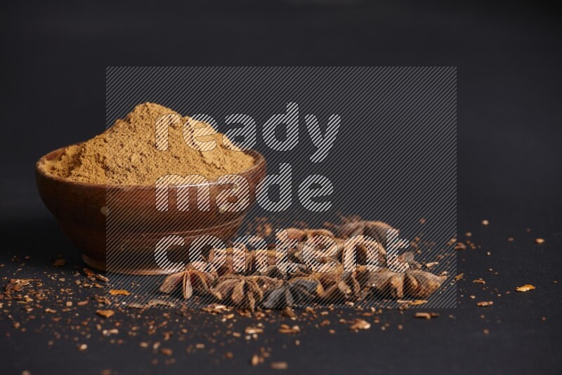 Star Anise powder in a wooden bowl with star anise beside it on a black background