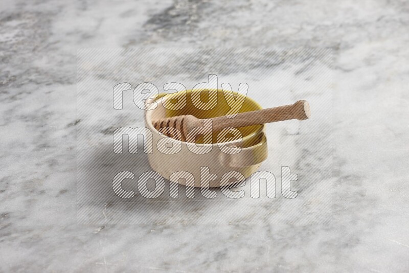 Multicolored pottery bowl with wooden honey dipper in it on grey marble background