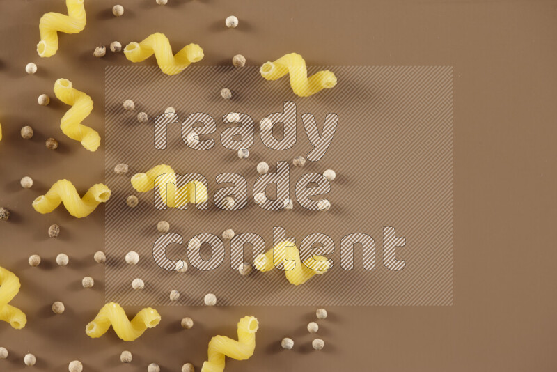 Raw pasta with different ingredients such as cherry tomatoes, garlic, onions, red chilis, black pepper, white pepper, bay laurel leaves, rosemary and cardamom on beige background