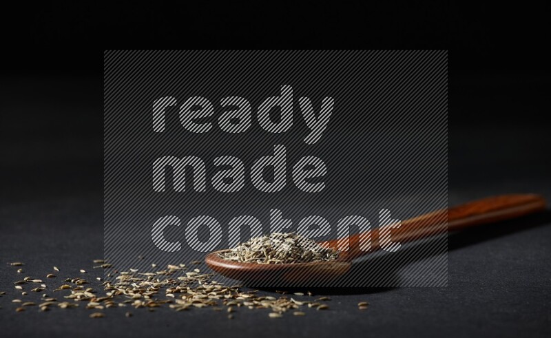 مغرفة خشبية ممتلئة بحبوب الكمون على خلفية سوداء