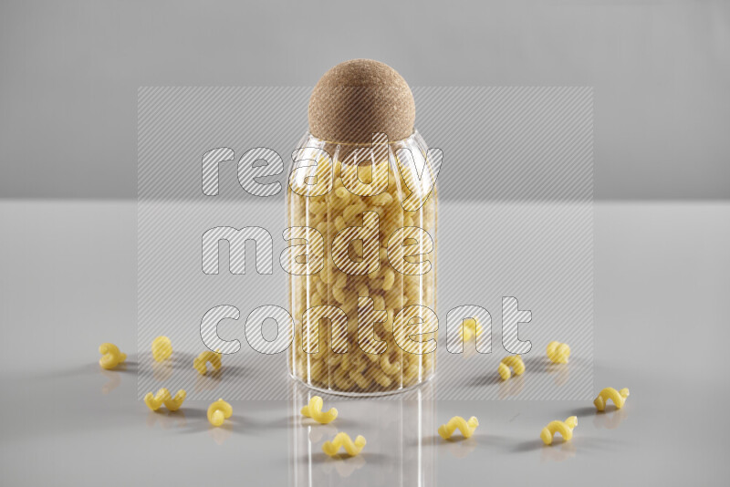 Raw pasta in a glass jar on light grey background