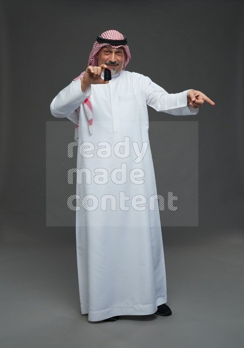 Saudi man with shomag Standing holding car key on gray background