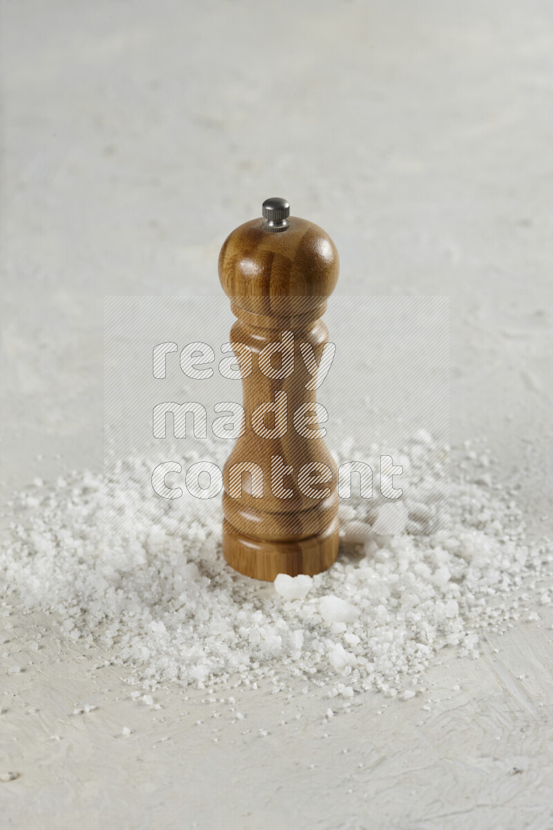 A wooden grinder standing upright and surrounded by coarse white seaa salt on white background