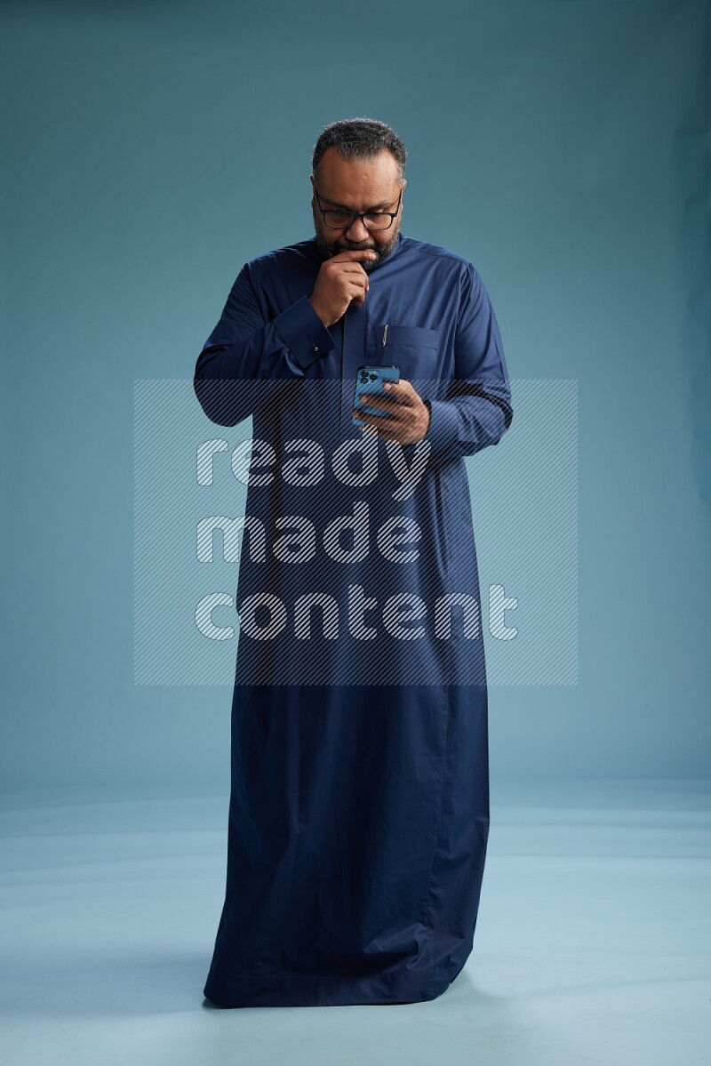 Saudi Man without shimag Standing texting on phone on blue background