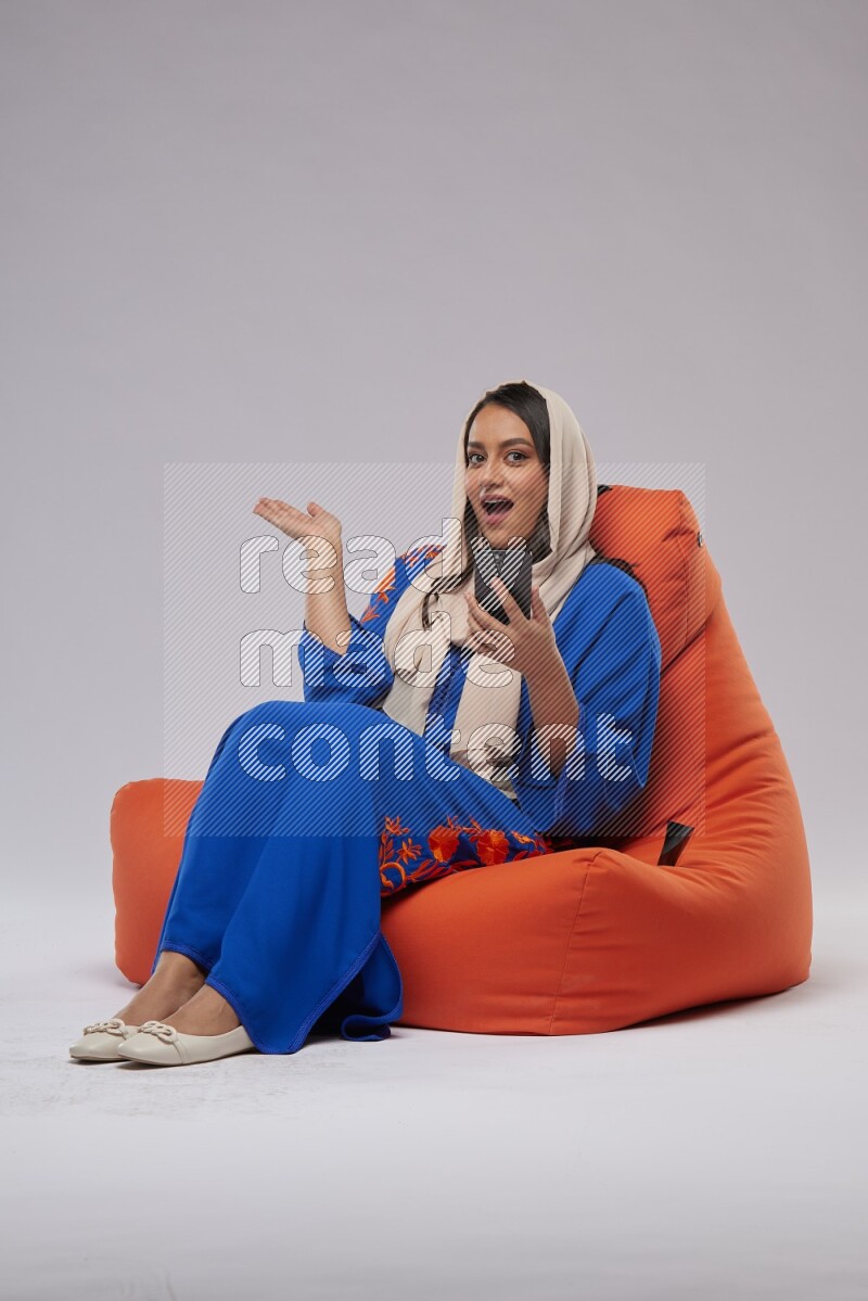 A Saudi woman sitting on an orange beanbag and texting on phone