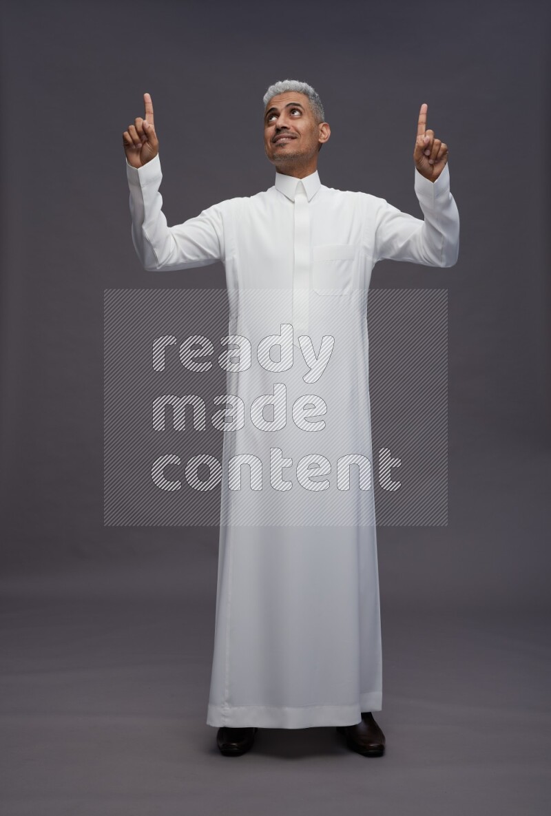 Saudi man wearing thob standing interacting with the camera on gray background
