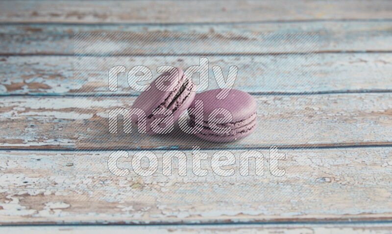 45º Shot of two Purple Blueberry macarons on light blue wooden background