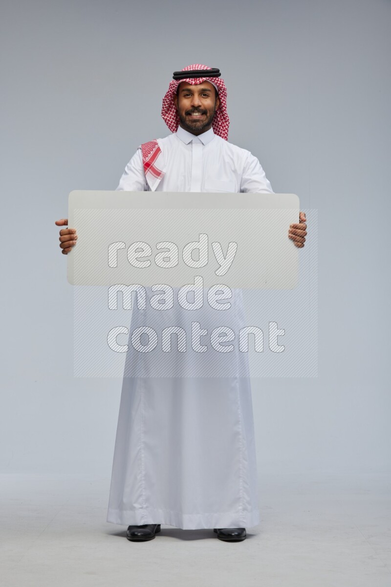 Saudi man Wearing Thob and shomag standing holding board on Gray background