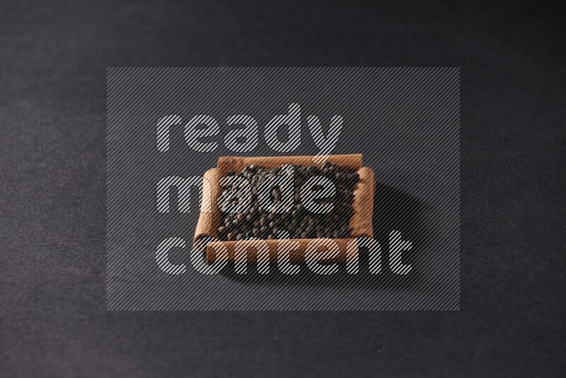 أربعة من أعواد القرفة مكونة شكل مربع بداخلها حبوب الفلفل الأسود علي خلفية سوداء