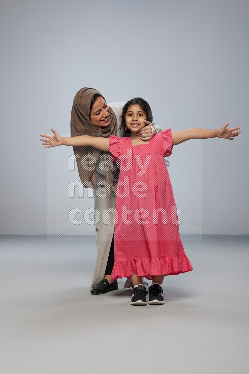 A girl and her mother interacting with the camera on gray background