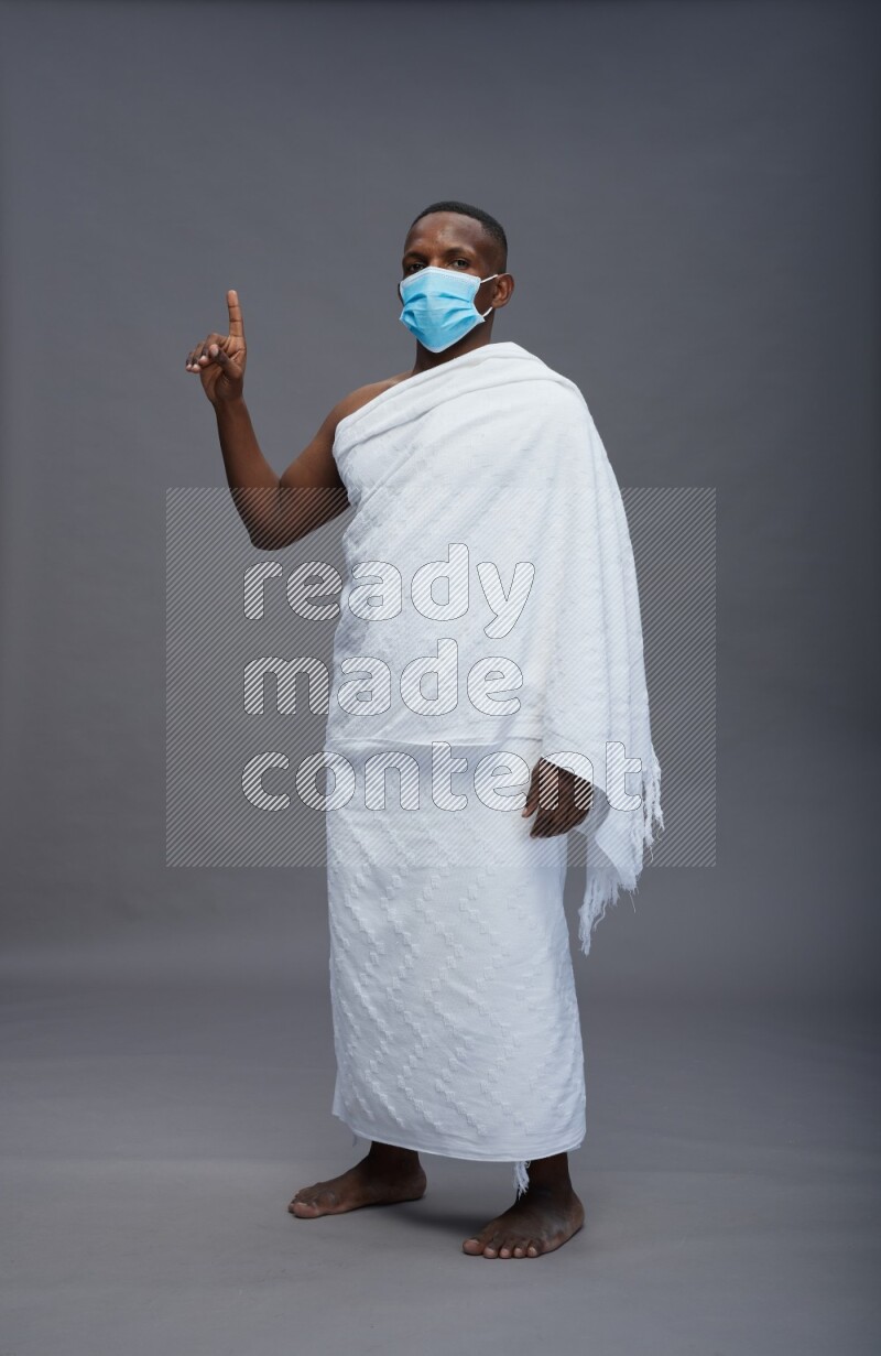 A man wearing Ehram with face mask Standing Interacting with the camera on gray background