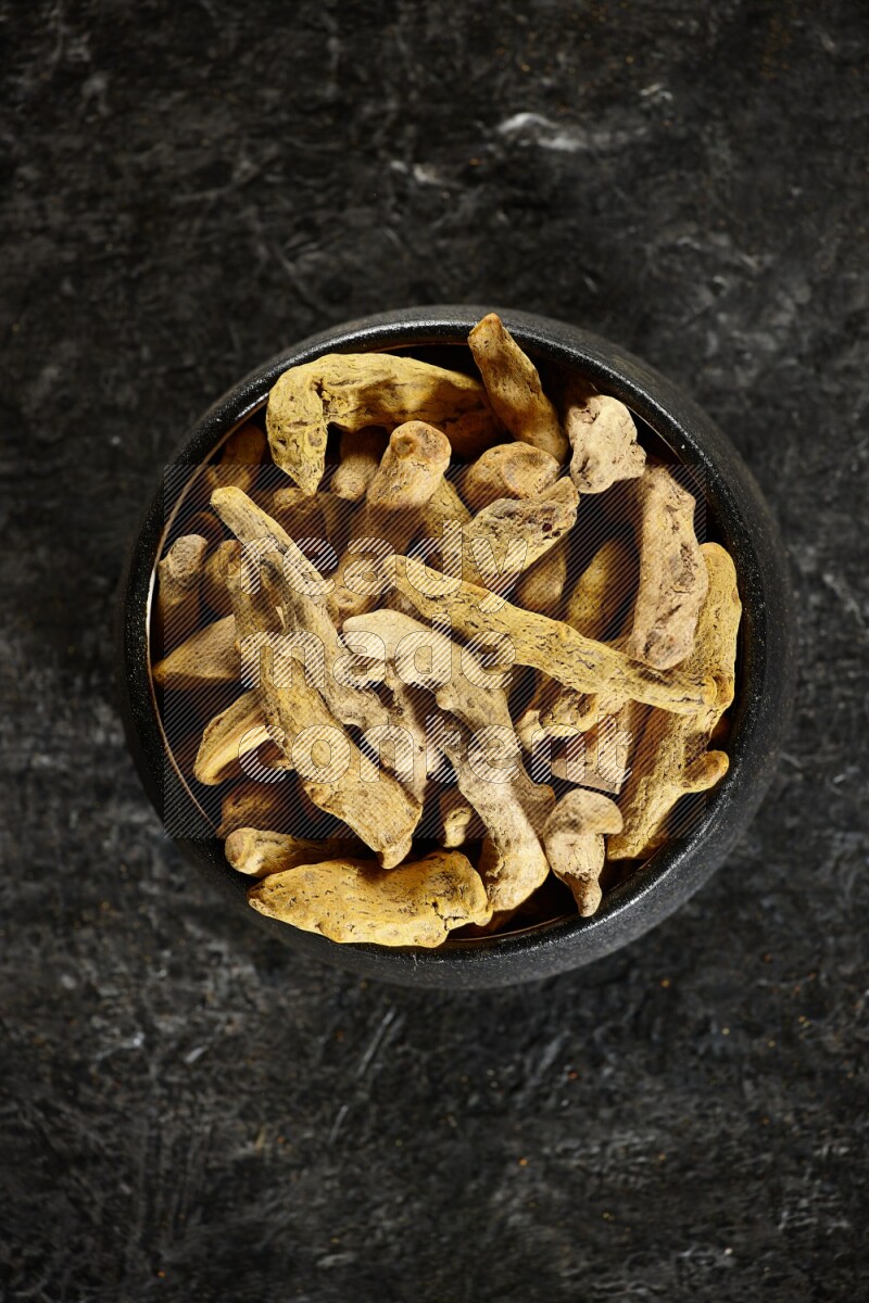 وعاء فخار أسود ممتلئ بأصابع كاملة من الكركم المجفف على خلفية سوداء