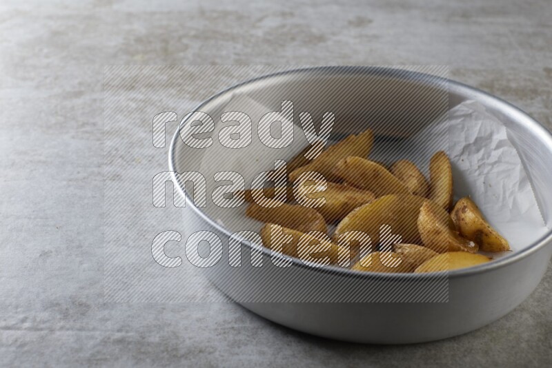 wedges potato on parchment paper in a stainless steel round tray on grey textured counter top