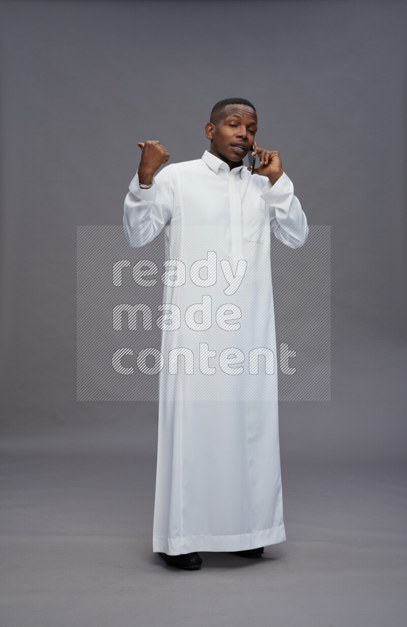 Saudi man wearing thob standing talking on phone on gray background