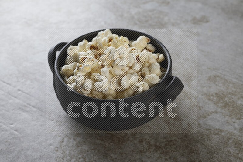 popcorn in a black handheld ceramic bowl on a grey textured countertop