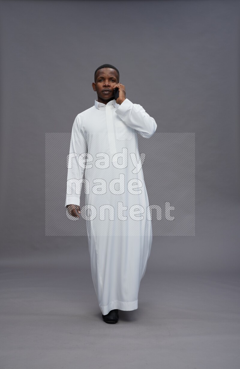Saudi man wearing thob standing talking on phone on gray background