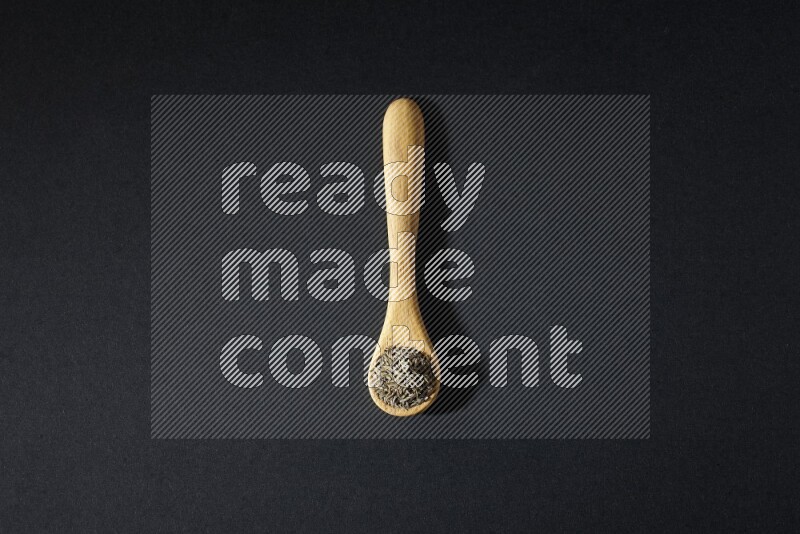 A wooden spoon full of cumin seeds on black flooring