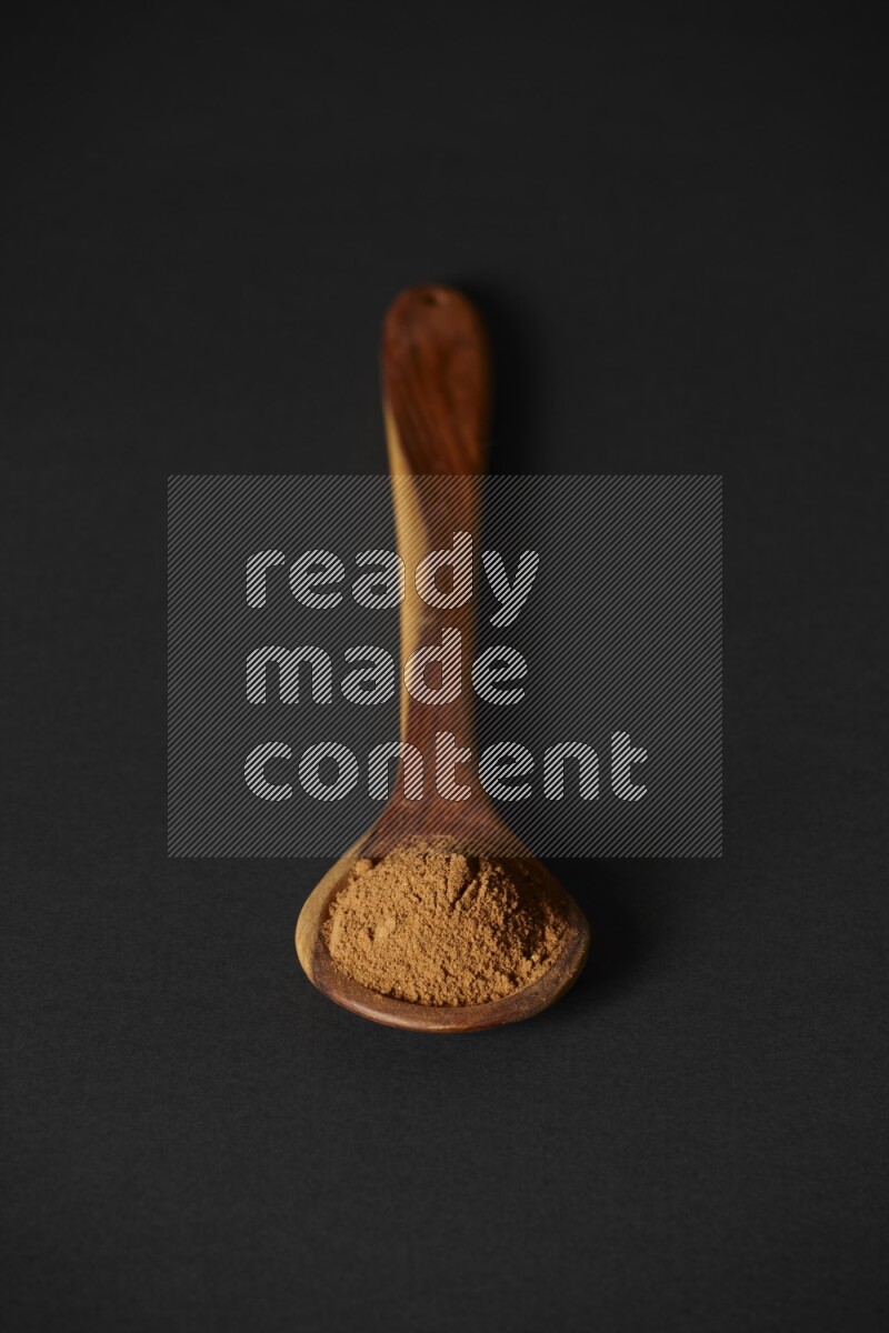 Cinnamon powder in a spoon ladle on black background