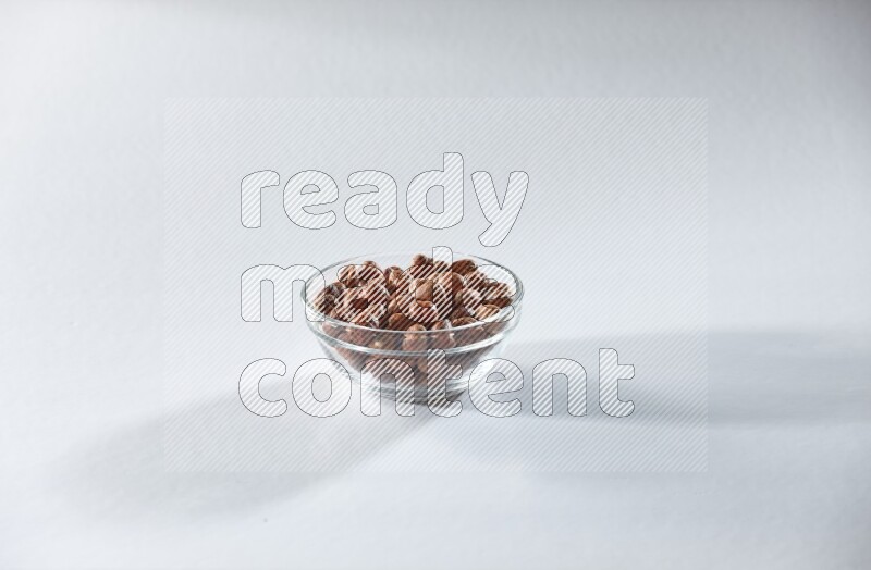 A glass bowl full of peeled hazelnuts on a white background in different angles