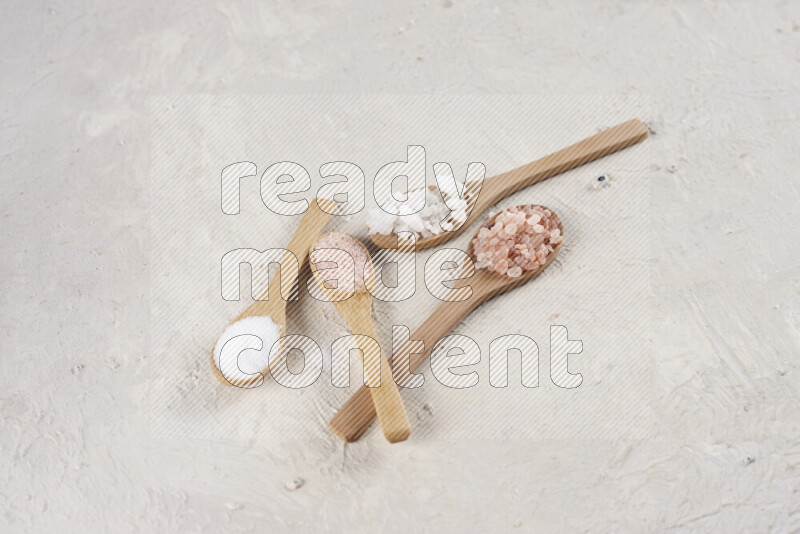 4 wooden spoons filled with fine and coarse salt on white background