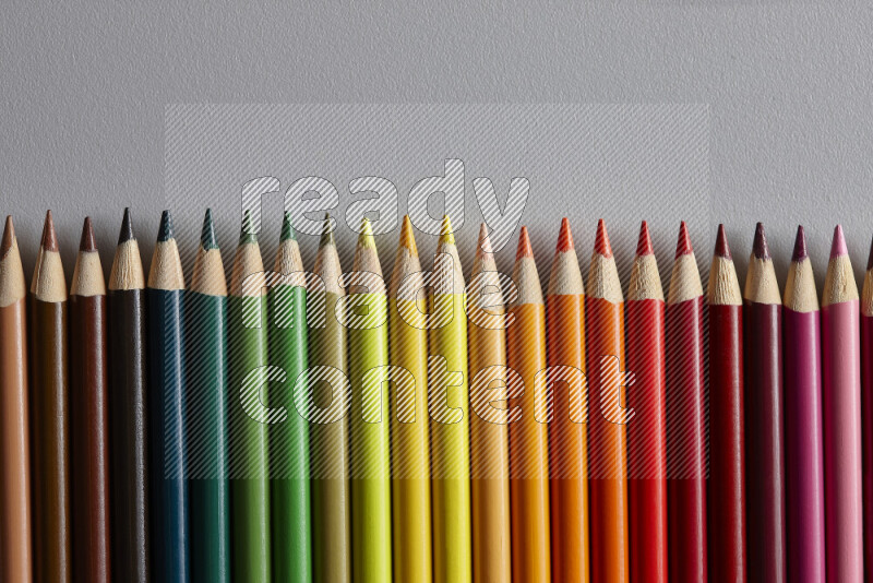 A collection of colored pencils arranged showcasing a gradient of different hues on grey background