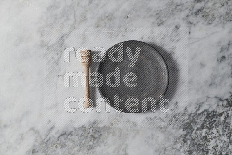 Black pottery plate with wooden honey dipper on the side on grey marble background