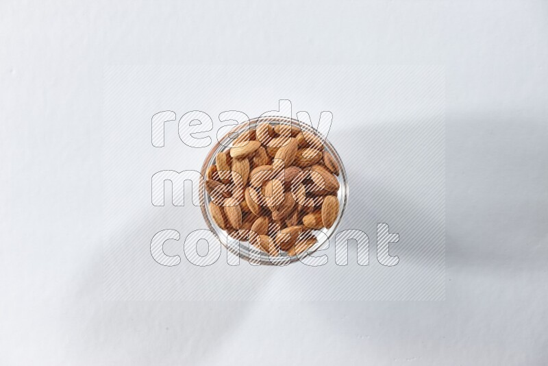 A glass bowl full of peeled almonds on a white background in different angles