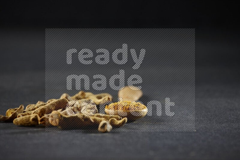 ملعقة خشبية ممتلئة ببودرة الكركم مع أصابع الكركم المجففة على خلفية سوداء