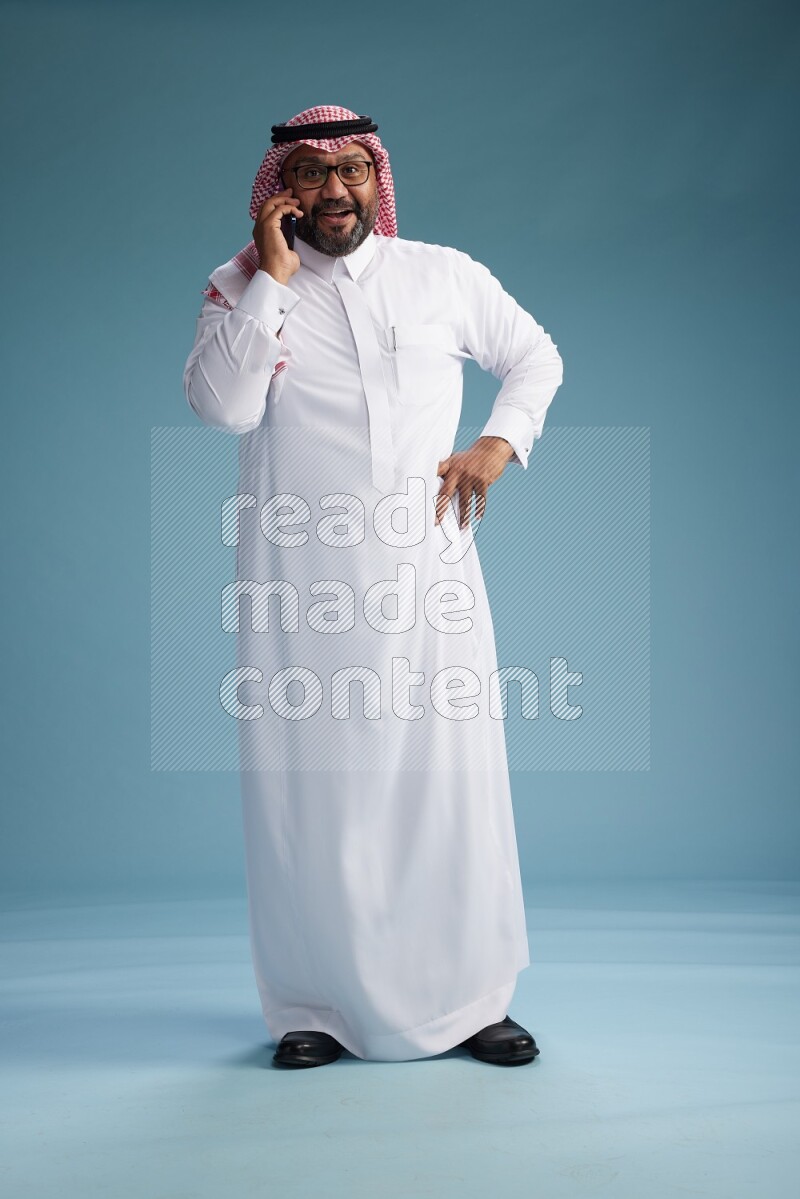 Saudi Man with shimag Standing talking on phone on blue background