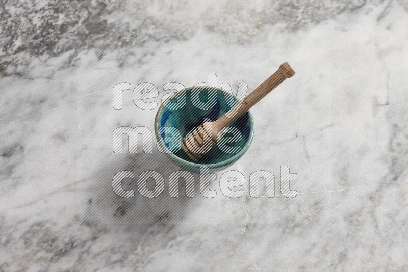 Decorative pottery bowl with wooden honey dipper in it on grey marble background