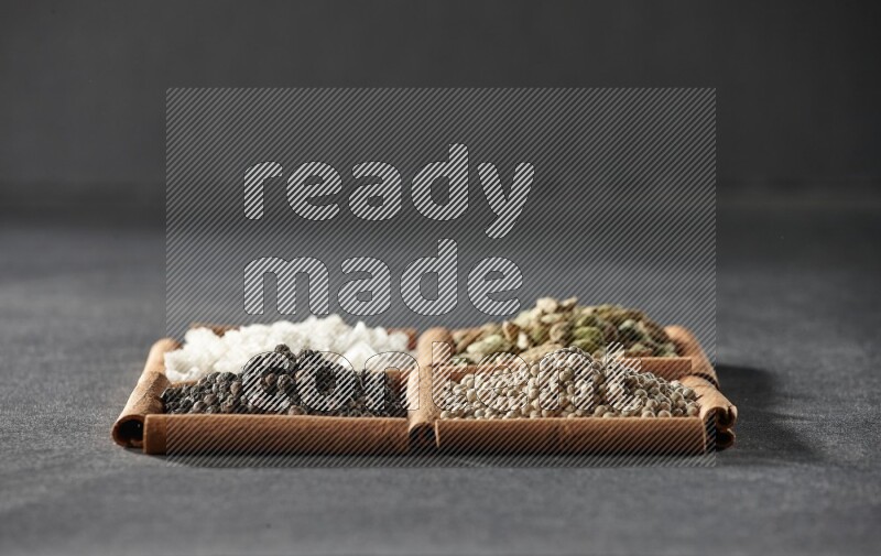 4 مربعات من عيدان القرفة ممتلئة بحبوب الفلفل الأسود والفلفل الأبيض وحب الهيل والملح الأبيض على أرضية سوداء