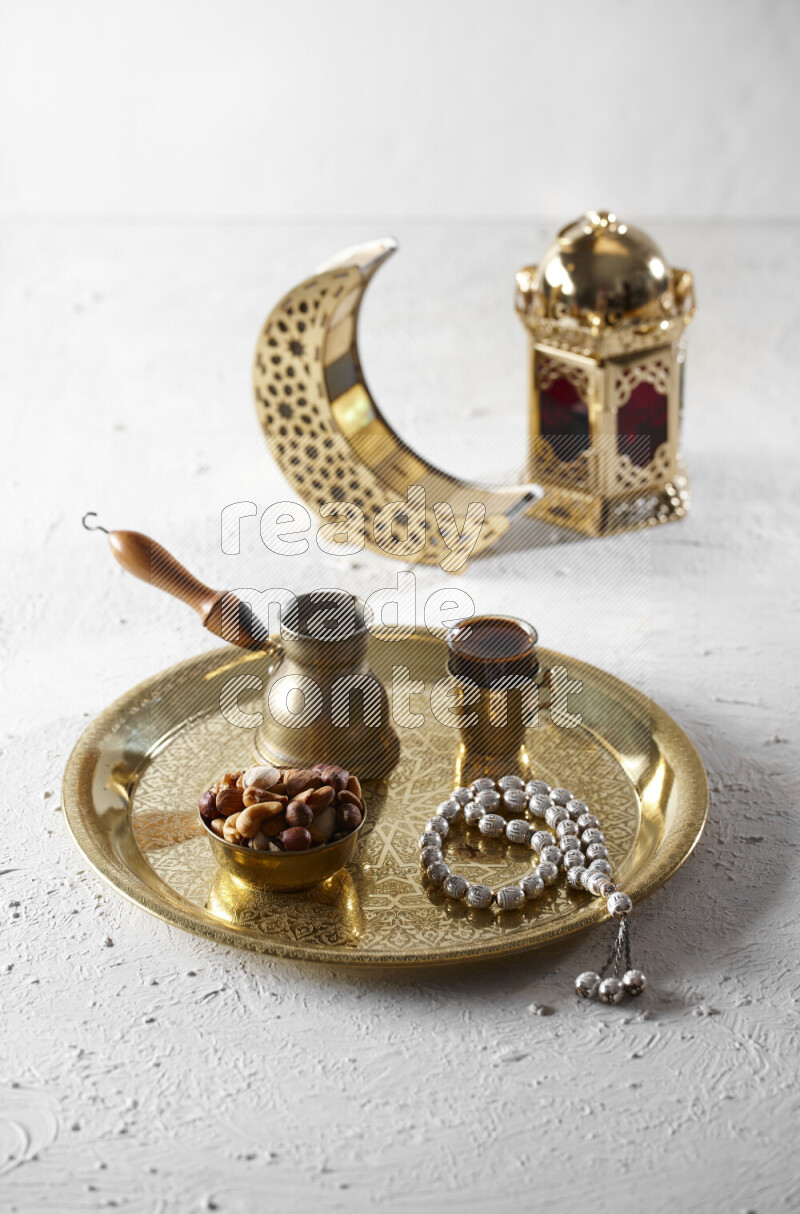 Nuts in a metal bowl with coffee and prayer beads on a tray beside lanterns in a light setup