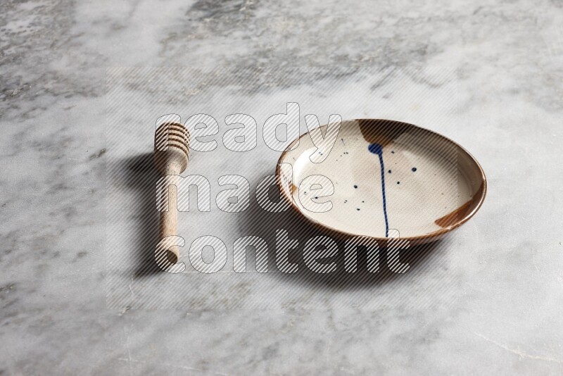 Multicolored pottery plate with wooden honey dipper on the side on grey marble background
